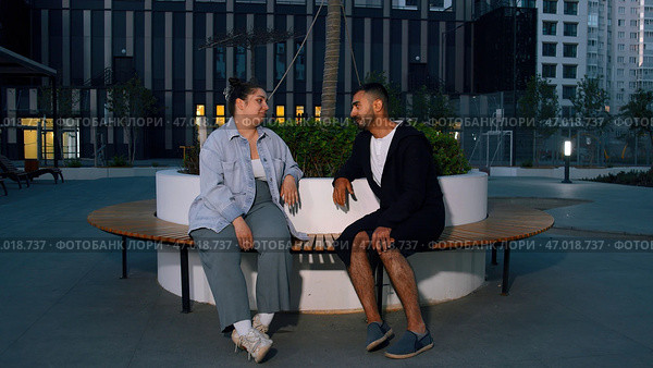 Friends man and woman sitting on wooden bench in a courtyard in new city region. Стоковое фото, фотограф David Kashakhi / Фотобанк Лори