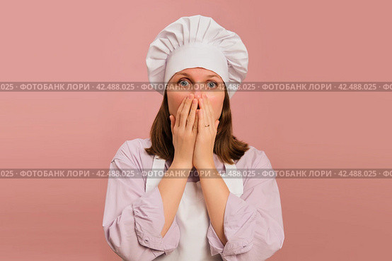 Frightened woman cook on studio pink background. Portrait of a female person in chef's clothing. Стоковое фото, фотограф Андрей Журавлев / Фотобанк Лори