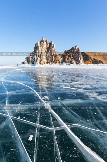 Frozen Baikal Lake. Winter travels to famous Shamanka Rock or Cape Burkhan - natural landmark of Olkhon Island. Scenic winter landscape with blue clear ice with cracks on sunny day in February. Стоковое фото, фотограф Виктория Катьянова / Фотобанк Лори