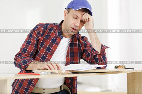 frustrated man reading instruction and putting together self assembly furniture. Стоковое фото, агентство Ingram Publishing / Фотобанк Лори