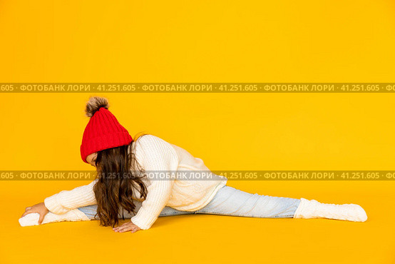 Funny child girl in a white sweatshirt and red knitted hat with pompom doing twine on a yellow background. The concept of children's emotions, joy and delight. Advertising clothing and sales. Стоковое фото, фотограф Ирина Михайличенко / Фотобанк Лори