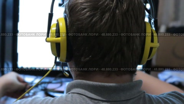 Геймер со спины в желтых наушниках сидит перед монитором с видео игрой в комнате. Крупный план. Стоковое видео, видеограф Александр Собко / Фотобанк Лори