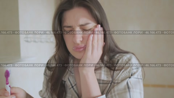 Girl brushes her teeth but feels pain, holding her cheek. Despite toothache, she continues caring for her oral health. Стоковое видео, видеограф Svetlana Golovco / Фотобанк Лори