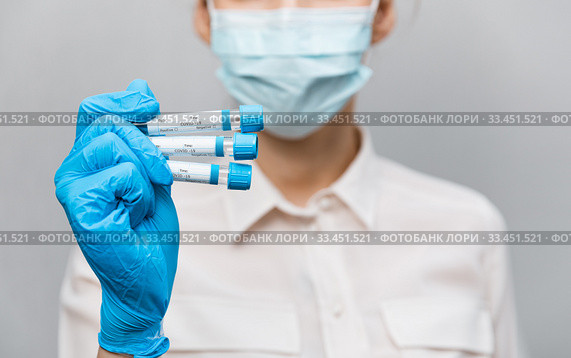 Girl Doctor in medical mask and rubber gloves, holds in her hands, closeup of test tube with tests for the presence of covid-19. Doctor in medical clothes demonstrates test tubes with coronavirus. Стоковое фото, фотограф Сергей Тимофеев / Фотобанк Лори