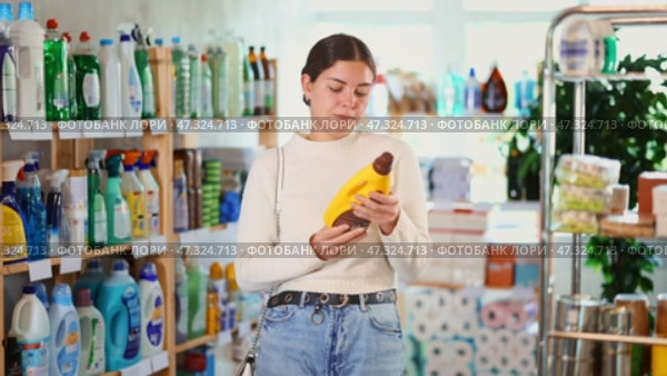 Girl housewife in household store examines and chooses polishing agent for wooden furniture, parquet. Стоковое видео, видеограф Яков Филимонов / Фотобанк Лори