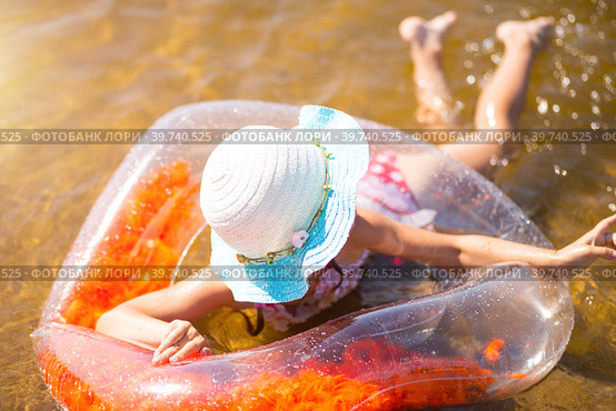Girl in a hat swimming in the river with a transparent inflatable circle in the shape of a heart with orange feathers inside.The sea with a sandy bottom. Beach holidays, swimming, tanning, sunscreens. Стоковое фото, фотограф Ольга Симонова / Фотобанк Лори