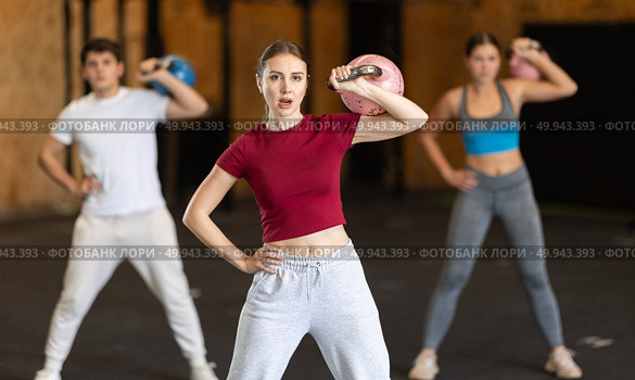 Girl in gym does exercises with kettlebell, lifts and lowers heavy kettlebell with one hand. Стоковое фото, фотограф Яков Филимонов / Фотобанк Лори