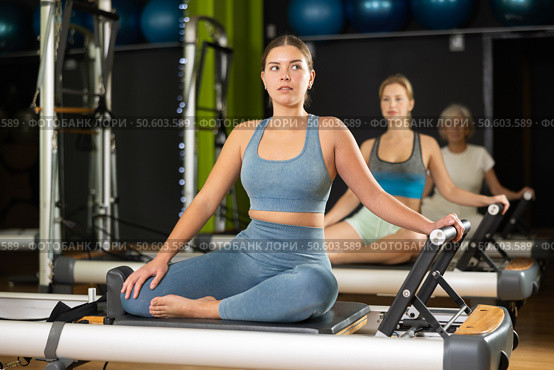 Girl sitting on foldable bed reformer performs exercises, strengthening body and muscles. Стоковое фото, фотограф Яков Филимонов / Фотобанк Лори