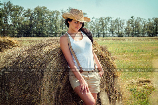 girl with black hair in beige wool coats and suspenders stands near the haystacks. Стоковое фото, агентство Ingram Publishing / Фотобанк Лори