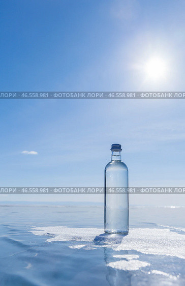 Glass bottle with cold natural drinking water stands on ice of frozen Baikal Lake on cold sunny winter day. Advertising and branding of drinking fresh ecological water. Nature background. Copy space. Стоковое фото, фотограф Виктория Катьянова / Фотобанк Лори