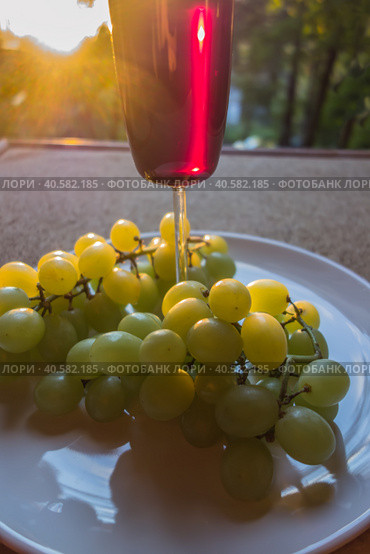 Glass of red wine and a bunch of white grapes at sunset. Стоковое фото, фотограф Iva Noel / Фотобанк Лори