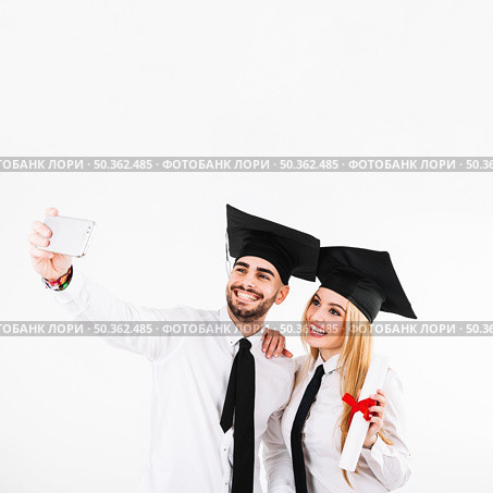 graduating couple mortarboards taking selfie. Стоковое фото, агентство Ingram Publishing / Фотобанк Лори