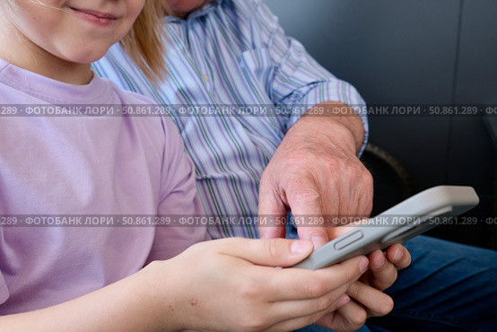 Granddaughter showing smartphone to grandfather. Portrait of a cute girl playing or typing on her smartphone while sitting in a cafe with her grandfather. Стоковое фото, фотограф Терехова Марина / Фотобанк Лори