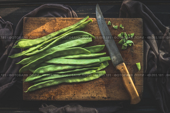 Green french beans on rustic cutting board with kitchen knife on dark wooden background, top view.  Legumes vegetables. Стоковое фото, агентство Ingram Publishing / Фотобанк Лори