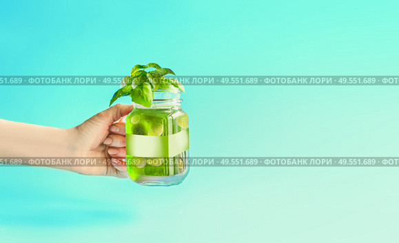 Green summer drink, lemonade with cucumber and lemon slices, flavored with herbs in Mason jar in female women hand at mint turquoise background. Summer mood. Healthy beverage. Infused water. Стоковое фото, агентство Ingram Publishing / Фотобанк Лори