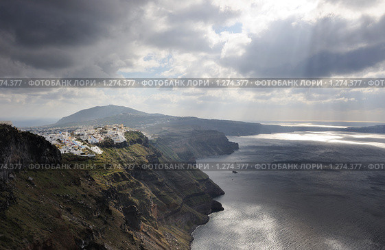 Греция. Эгейское море. Остров Санторини ( Santorni ). Вид на отвесные разноцветный склоны кальдеры потухшего вулкана, город Фира и море под светом яркого солнца, пробивающегося лучами из-под облаков (2008 год). Стоковое фото, фотограф Дмитрий Заморин / Фотобанк Лори