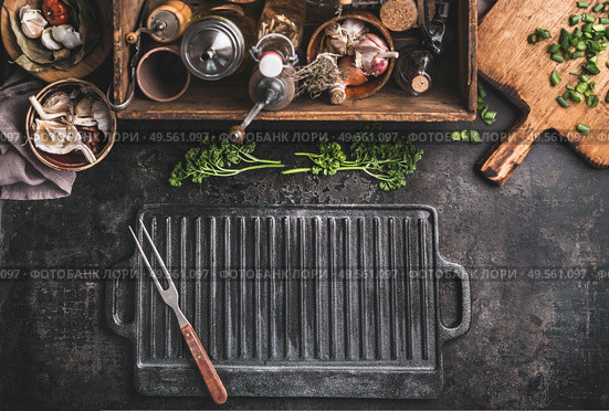 Grill or BBQ food background with empty cast iron grill griddle and meat fork  on roast rustic kitchen table. Wooden box with seasonings, oils and other kitchen utensils.Top view. Place for design. Стоковое фото, агентство Ingram Publishing / Фотобанк Лори
