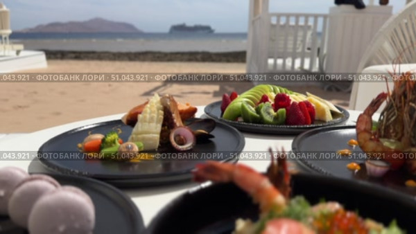Grilled salmon steak with crispy skin sauteed vegetables and lemon served in outdoor restaurant in summer light A wooden table with a variety of dishes containing seafood, vegetables and fruit.Hand holding a spoon ready to eat pineapple fried rice with shrimp, served in a pineapple bowl, surrounded by fresh fruits and tea on a cozy table setting.Party Sea Food platter with salmon and prawns, low angle view, close-up Sea food party platter, extreme Whole poached salmon with cucumber slices for scales, high end party platter, overhead view Tiger prawns on the grill Macarooni cookies floating on blue background, levitation, macarooni cookies, dessert, sweets, colorful, delicious Two Glasses of Pink Champagne with Macarons and Oranges Elegant seaside celebration with seafood, pink floral decor, and sparkling wine overlooking the ocean. Стоковое видео, видеограф Zita Khasanova / Фотобанк Лори