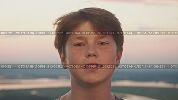 Grinning adolescent with red hair and freckles, standing against the backdrop of a sunset on a summer afternoon. Стоковое видео, видеограф Strunov David / Фотобанк Лори