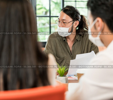 Group of asian business person team meeting and brainstorm in meeting room after office reopen, they wear protective face mask as new normal practice to prevent coronavirus infection. Стоковое фото, агентство Ingram Publishing / Фотобанк Лори