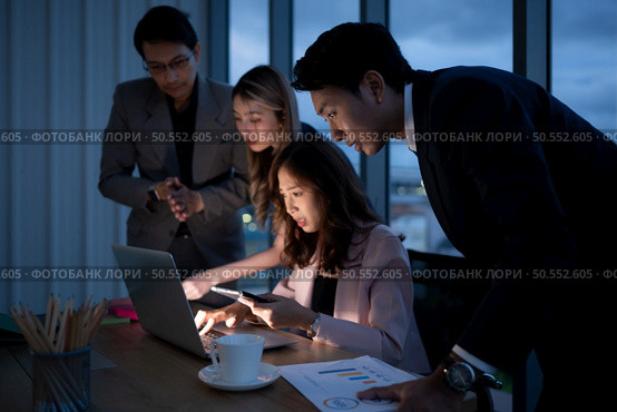 Group of broker international stock traders working actively at night in office, A young woman is working hustle to present a client with friends helping her with information. Стоковое фото, агентство Ingram Publishing / Фотобанк Лори