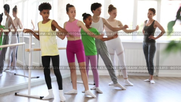 Group of concentrated teenage students of ballet school diligently practicing Demi rond de jambe par terre at barre in sunlit mirrored choreographic studio to applause of smiling female choreographer. Стоковое видео, видеограф Яков Филимонов / Фотобанк Лори