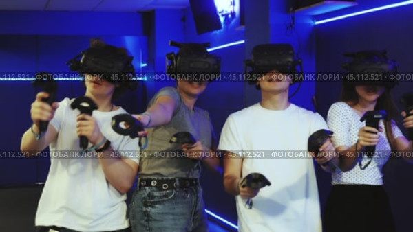 Group of excited young people with handheld controllers in hands engaged in virtual world experiencing through VR glasses covering face. Concept of immersion and interactivity in game. Стоковое видео, видеограф Яков Филимонов / Фотобанк Лори