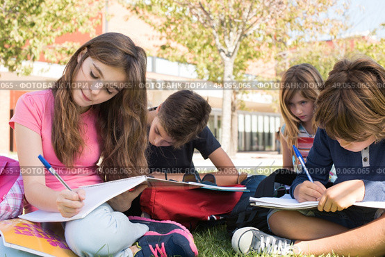 Group of little students sitting on the grass at school. Стоковое фото, агентство Ingram Publishing / Фотобанк Лори