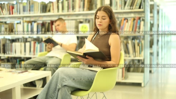 Group of students reading and discussing books while sitting on chair in library. Стоковое видео, видеограф Яков Филимонов / Фотобанк Лори