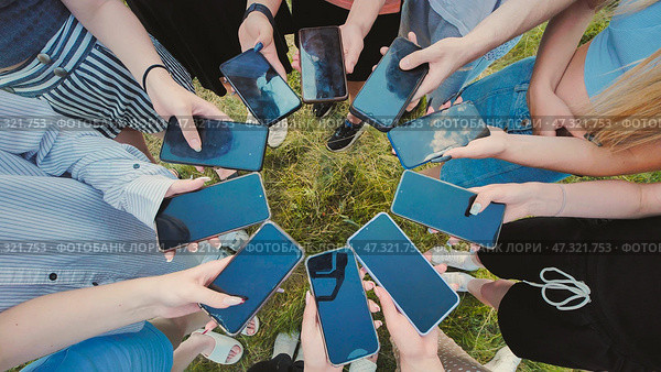 Group of students standing in a circle in the park, holding smartphones with blank screens while enjoying the outdoors together. Стоковое фото, фотограф Mikhail Davidovich / Фотобанк Лори