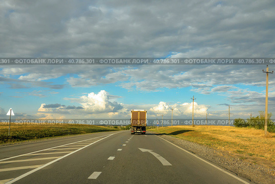 Грузовик, уезжающий вдаль по пустой асфальтированной дороге. Lone truck van receding along the asphalt road out of town toward the horizon. Beautiful blue sky with lots of clouds. Стоковое фото, фотограф Валерий Елистратов / Фотобанк Лори