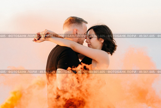 guy and a girl in black clothes hug and run on the white sand with orange smoke. Стоковое фото, агентство Ingram Publishing / Фотобанк Лори