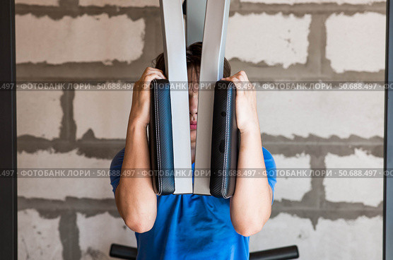 Gym. The picture shows a young man exercising his arms and back using a pull-up machine. Sports and a healthy lifestyle. Стоковое фото, фотограф Photojuli / Фотобанк Лори