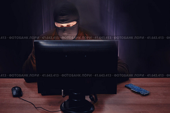 Hacker in balaclava steals information in the server room. Concept of data integrity issues and hacker attacks. Стоковое фото, фотограф Андрей Журавлев / Фотобанк Лори