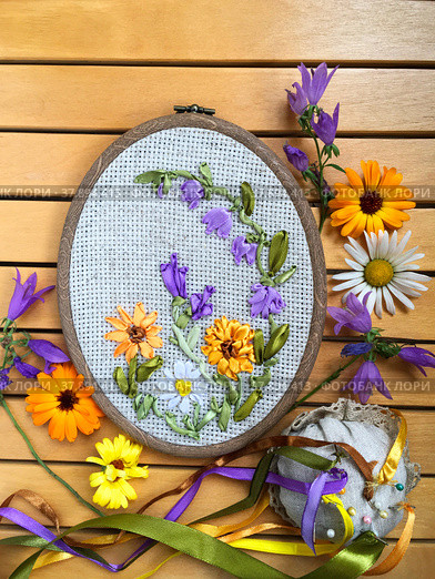 Hand embroidery with satin ribbons of a floral ornament with flowers of calendula, bluebells and daisies on a wooden background (embroidery was made by the author of the photo). Flat lay, closeup. Стоковое фото, фотограф Виктория Катьянова / Фотобанк Лори