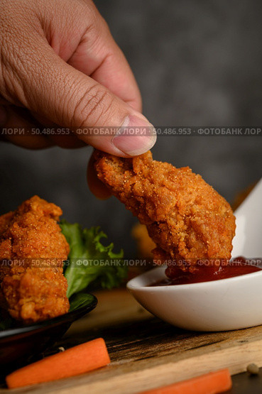Hand holding crispy fried chicken dipped in tomato sauce. Selective focus. Стоковое фото, агентство Ingram Publishing / Фотобанк Лори
