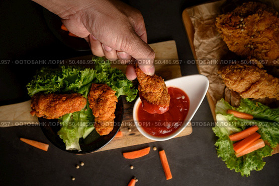 Hand holding crispy fried chicken dipped in tomato sauce. Selective focus. Стоковое фото, агентство Ingram Publishing / Фотобанк Лори
