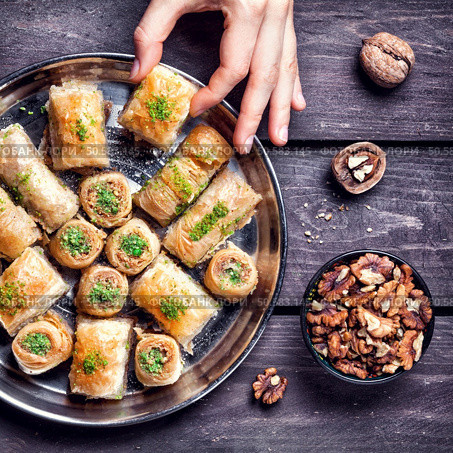 Hand holding Turkish baklava near walnuts on wooden background  . Стоковое фото, агентство Ingram Publishing / Фотобанк Лори