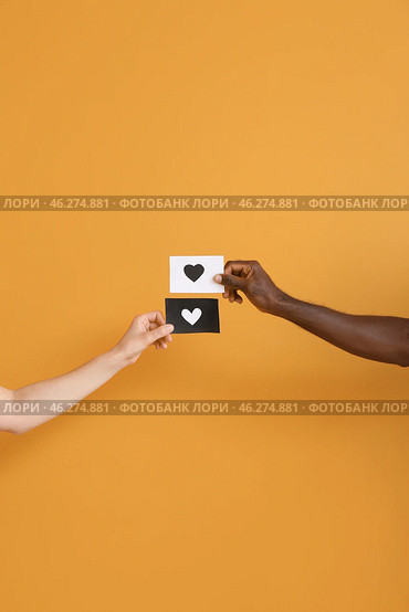 Hands of Caucasian woman and African-American man holding paper sheets with drawn heart on color background. Racism concept. Стоковое фото, фотограф Pixel_shot / Фотобанк Лори