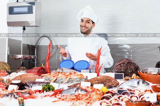 Handsome male chef standing behind icy showcase of fish restaurant, offering fresh seafood. Стоковое фото, фотограф Яков Филимонов / Фотобанк Лори