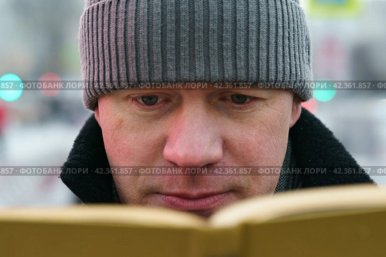 Handsome man in Moscow city center during coronavirus pandemic. New Year holidays. He sitting at the bench and reading the book in the public park. Стоковое фото, фотограф YuryKara / Фотобанк Лори