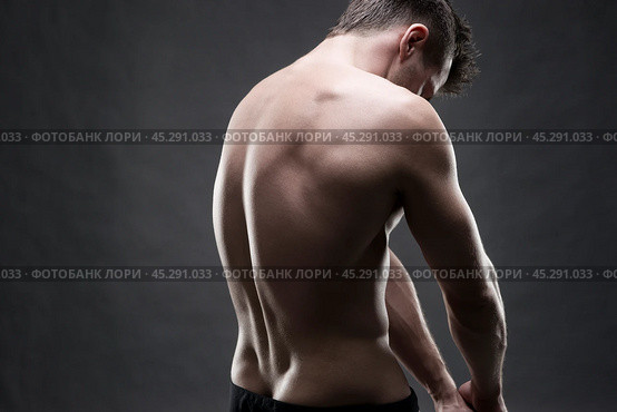 Handsome muscular bodybuilder posing on gray background. Low key studio shot. Стоковое фото, фотограф Станислав Тарко / Фотобанк Лори