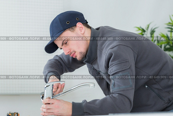 handsome young plumber fixing tap at cleints home. Стоковое фото, агентство Ingram Publishing / Фотобанк Лори