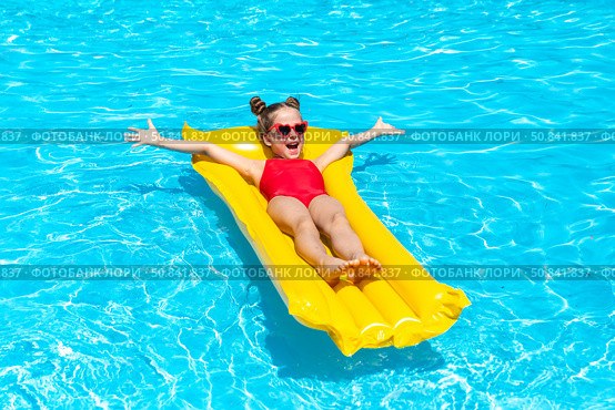 Happy little girl in red swimsuit lies comfortably on yellow inflatable mattress in swimming pool with blue water on warm summer day on tropical vacation. Happiness, freedom, childhood concept. Стоковое фото, фотограф Ирина Михайличенко / Фотобанк Лори