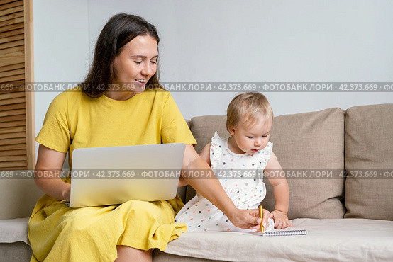 Happy mother taking notes for child while working from home. Multitasking due to maternity leave. Стоковое фото, фотограф Natalia Gdovskaia / Фотобанк Лори