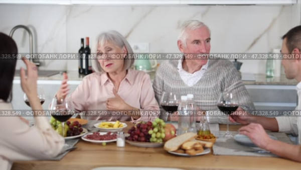 Happy senior parents and young couple talking while drinking wine sitting around kitchen table. Стоковое видео, видеограф Яков Филимонов / Фотобанк Лори