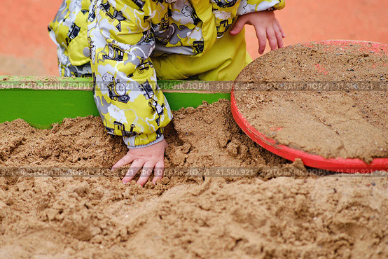 Happy toddler baby boy is playing in the sandbox. A child in warm clothes is playing with sand on the playground. Kid aged one year and two months in a yellow autumn jumpsuit. Стоковое фото, фотограф Андрей Журавлев / Фотобанк Лори