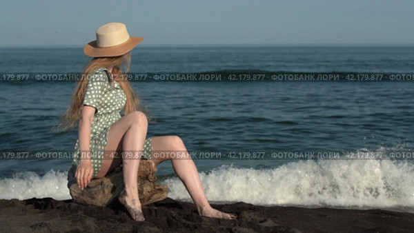 Happy young blonde woman turning around, sitting on log on beach on background of ocean waves. Стоковое видео, видеограф А. А. Пирагис / Фотобанк Лори