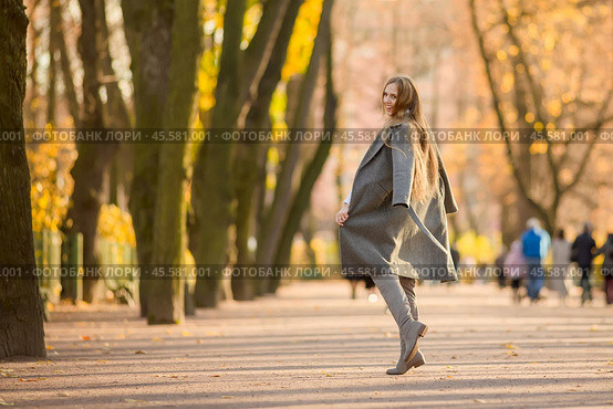 Happy young woman walks in the autumn park. An attractive woman with light brown hair and a gray coat is walking down the alley. Beautiful autumn mood. Fall season. Стоковое фото, фотограф Андрей Степанов / Фотобанк Лори