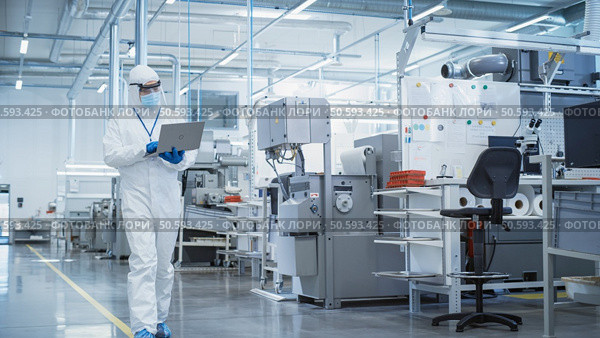 Heavy Industry Manufacturing Factory: Scientist in Sterile Coverall Walking with Laptop Computer, Examining Industrial CNC Machine Settings and Configuring Production Functionality. Стоковое фото, агентство Ingram Publishing / Фотобанк Лори